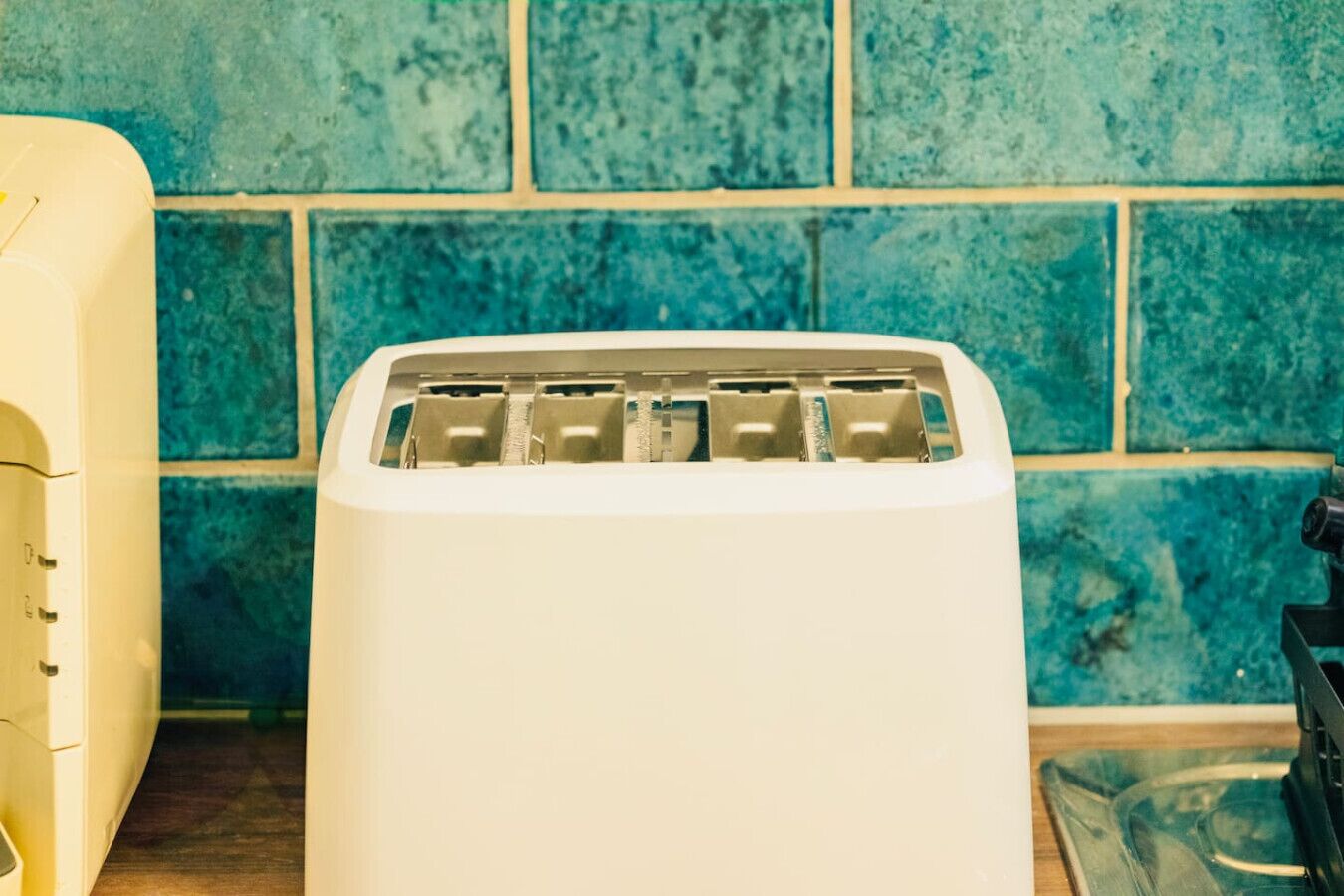 A white toaster with four slots against a blue tiled wall.