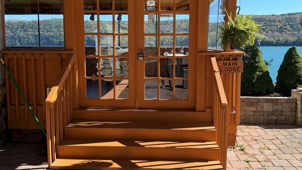Un chalet en bois doté d’une grande porte vitrée, d’une terrasse en briques et offrant une vue sur un lac.