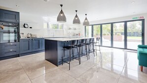 A modern kitchen with a central island, bar stools, and pendant lighting. - Mayrose House: 6BR 4BATH Luxe Spacious Retreat (Takeley)