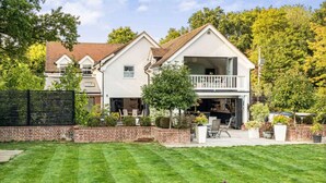 A two-story house with a covered patio and a well-maintained lawn. - Mayrose House: 6BR 4BATH Luxe Spacious Retreat (Takeley)