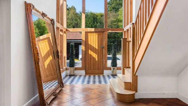 A spacious entryway with a wooden staircase, a large wooden door, and a checkered floor. - Mayrose House: 6BR 4BATH Luxe Spacious Retreat (Takeley)