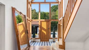 Un hall d’entrée spacieux avec un escalier en bois, une grande porte en bois et un sol à carreaux.