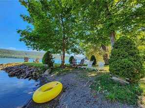 A lakeside setting with a yellow inflatable ring, outdoor seating, and a view of the lake. - Hatch's Perch - Quaint 2nd floor apt, private balcony, terrific lake views (Cooperstown)