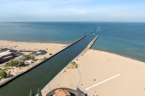 A coastal area with a beach, a pier, and a road leading to a parking area.