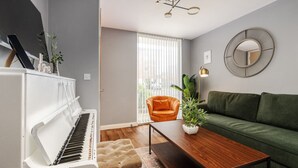 En stue med et klaver, en grøn sofa, en orange lænestol og et træbord.