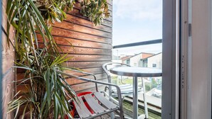 En balkon med en metalstol og et bord, træpaneler og udsigt til bygninger.