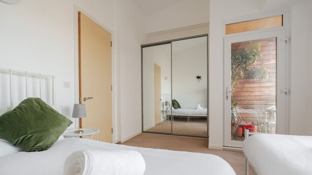 Et hotelværelse med en seng, en grøn pude, et hvidt håndklæde, et lille bord med en lampe og en skydedør til en balkon med en stol og plantekasser.