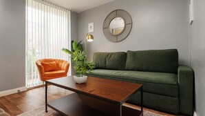 En stue med en grøn sofa, en orange lænestol, et træsofabord, en gulvlampe og en potteplante.