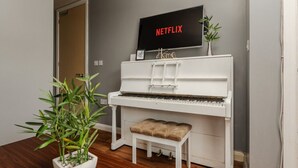 Et hvidt klaver med bænk, en potteplante og et vægmonteret TV, der viser 'NETFLIX' og 'Hjem'.