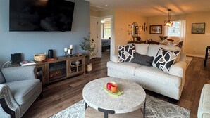 Ein Wohnzimmer mit grauem Sofa, rundem Couchtisch, Flachbildfernseher und Kamin.
