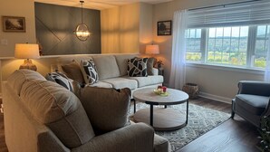 Ein Wohnzimmer mit Sofa, Sesseln, einem Couchtisch und Blick ins Freie durch ein Fenster.