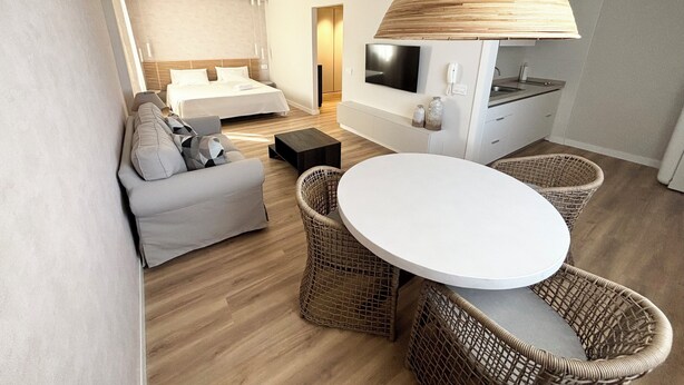 Een moderne hotelkamer met een bed, een slaapbank, een eettafel, rieten stoelen, een televisie en een keukenhoek.