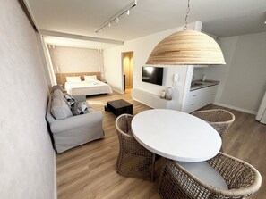 A modern hotel room with a bed, a sofa, a dining table, wicker chairs, a TV, and a kitchen area. - Studio with a Pool in Downtown Santa Cruz (SANTA CRUZ DE TENERIFE)