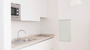 Een moderne keuken met witte kasten, een RVS-spoelbak, een magnetron en een hanglamp.