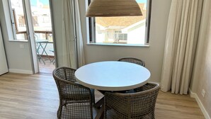 Een kamer met een ronde tafel, rieten stoelen, een hanglamp en uitzicht door een raam.