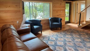 Una habitación acogedora con un sofá de cuero marrón, dos sillones azul oscuro y una alfombra estampada.