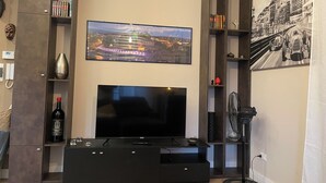 A modern living room with a large flat-screen TV mounted on a wall, a built-in entertainment unit below, and a large framed cityscape picture on the right. - Cozy apartment in the center of Cosenza equipped with every comfort (Cosenza)