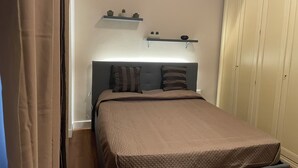 A bedroom with a bed, a headboard, a wardrobe, and two shelves with decorative items. - Cozy apartment in the center of Cosenza equipped with every comfort (Cosenza)