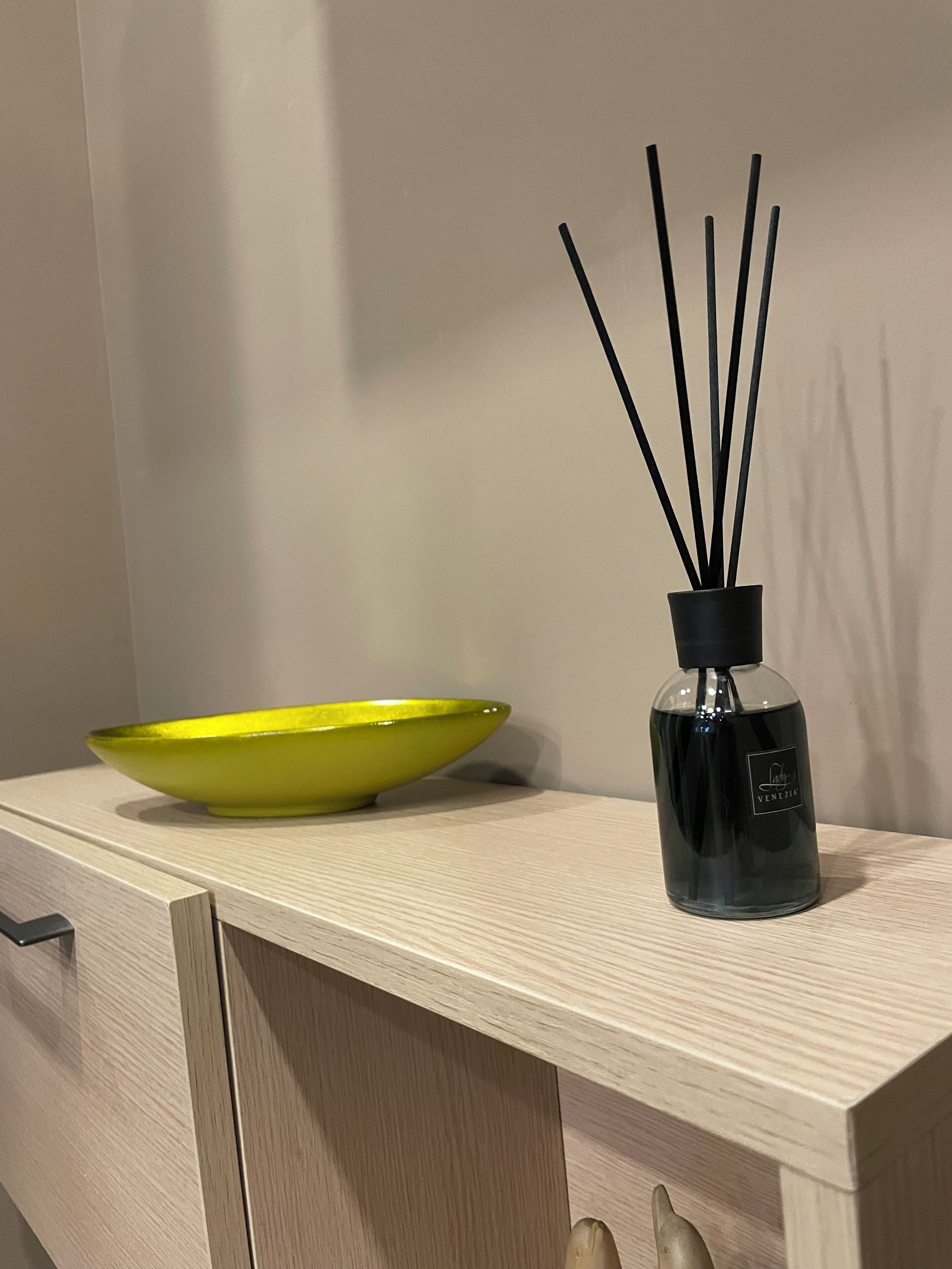 A wooden cabinet with a yellow bowl and a black bottle with black sticks on top.
