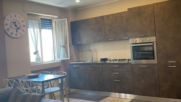 A modern kitchen with dark cabinets, a built-in oven, and a dining area with a sofa and chairs. - Cozy apartment in the center of Cosenza equipped with every comfort (Cosenza)
