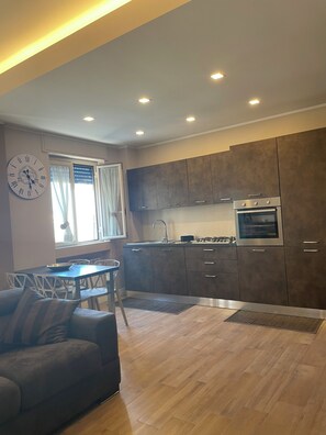 A modern kitchen with dark cabinets, a built-in oven, and a dining area with a sofa and chairs. - Cozy apartment in the center of Cosenza with all the amenities (Cosenza)