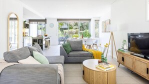 Un salon moderne avec un canapé gris, une table basse ronde et un téléviseur posé sur un meuble en bois.
