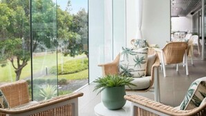 Une pièce meublée de mobilier en osier, agrémentée d’une plante en pot, et offrant une vue sur un jardin grâce à de grandes fenêtres.