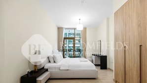 Une chambre moderne avec un grand lit, des tables de chevet, une armoire et une vue sur la ville grâce à de grandes fenêtres.