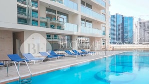 Une piscine avec des chaises longues bleues et un bâtiment moderne doté de balcons en arrière-plan.