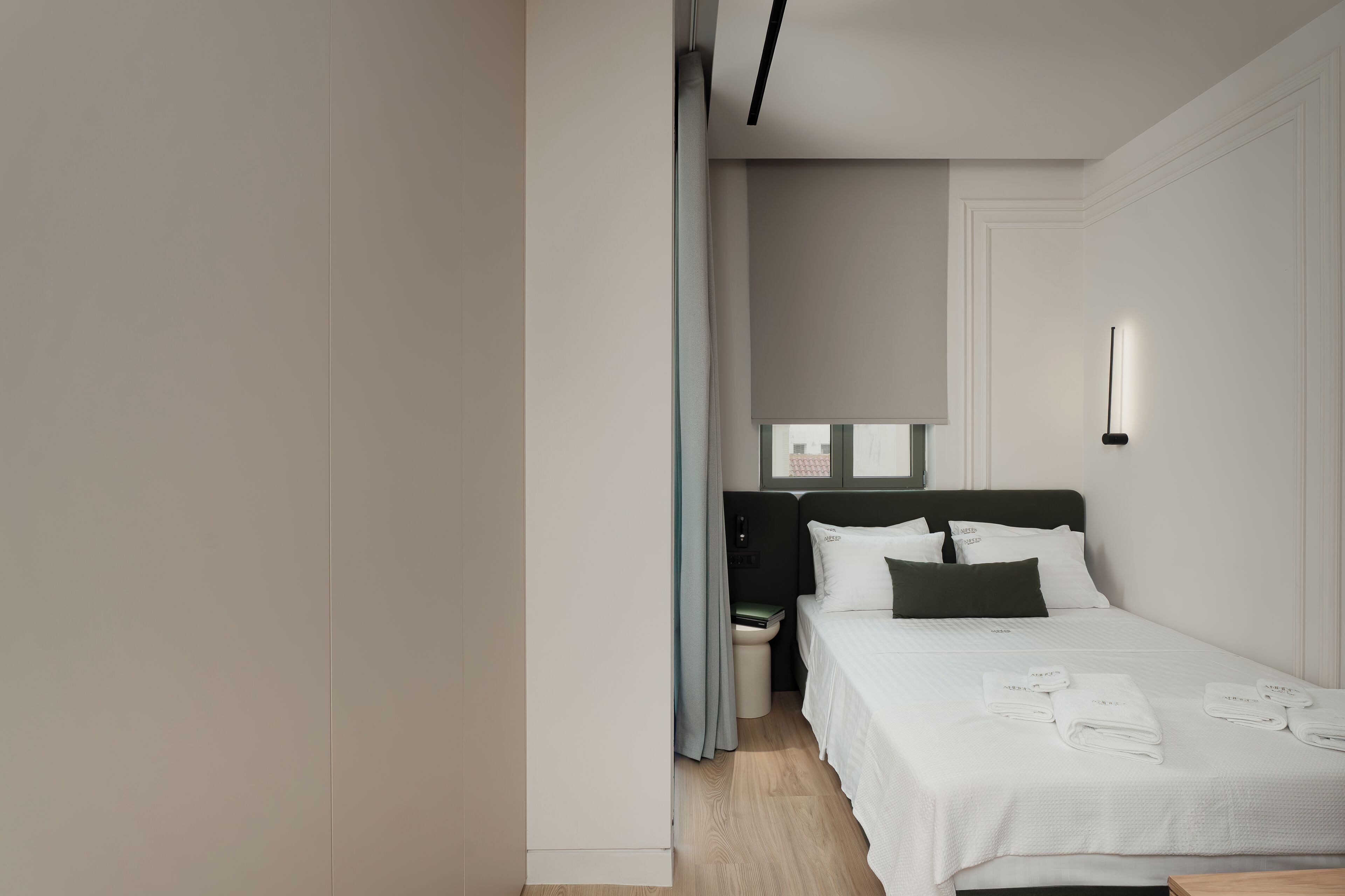 Moderni hotellihuone, jossa on siististi pedattu sänky, yöpöytä ja pieni sivupöytä.