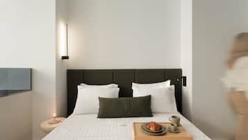 Ein modernes Hotelzimmer mit einem großen Bett, einem Nachttisch mit Lampe sowie einem Tablett mit Croissant und Kaffeetassen.