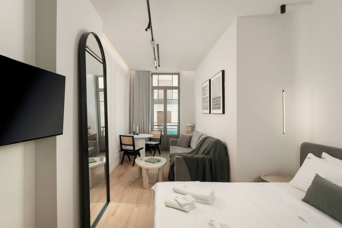 A modern hotel room with a bed, a desk, a chair, and a large mirror.