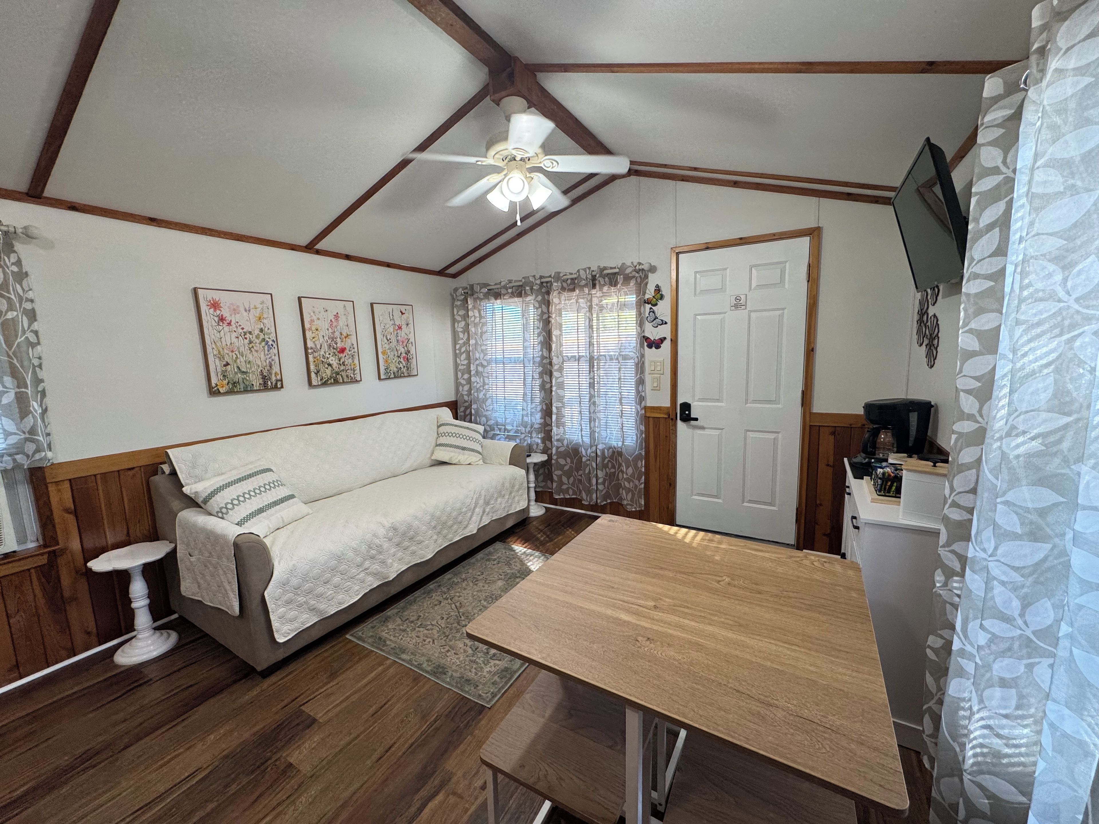 Quarto acolhedor com teto de madeira, uma cama, uma mesa pequena e uma TV na parede.