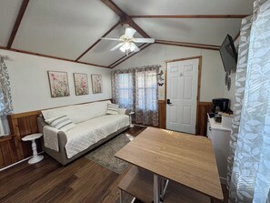 A cozy room with a wooden ceiling, a bed, a small table, and a TV mounted on the wall. - Cabin 2: Cozy Tiny Cabin, Sleeps 4, Pet Friendly (Checotah)