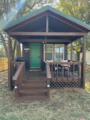 Une structure en bois avec une porte verte, une véranda et une table entourée de chaises.