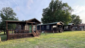 A row of cabins with wooden decks and porches, surrounded by a grassy field and trees. - Boulder Ridge Cabin 2: The Cottage - Newly Renovated Tiny Cabin Sleeps 4 (Checotah)