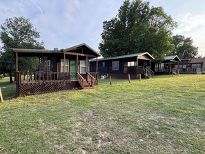 A row of cabins with wooden decks and porches, surrounded by a grassy field and trees. - Boulder Ridge Cabin 2: The Cottage - Newly Renovated Tiny Cabin Sleeps 4 (Checotah)