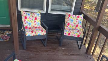 Een overdekte buitenruimte met rieten stoelen en een tafel, omgeven door ramen en een houten terras.