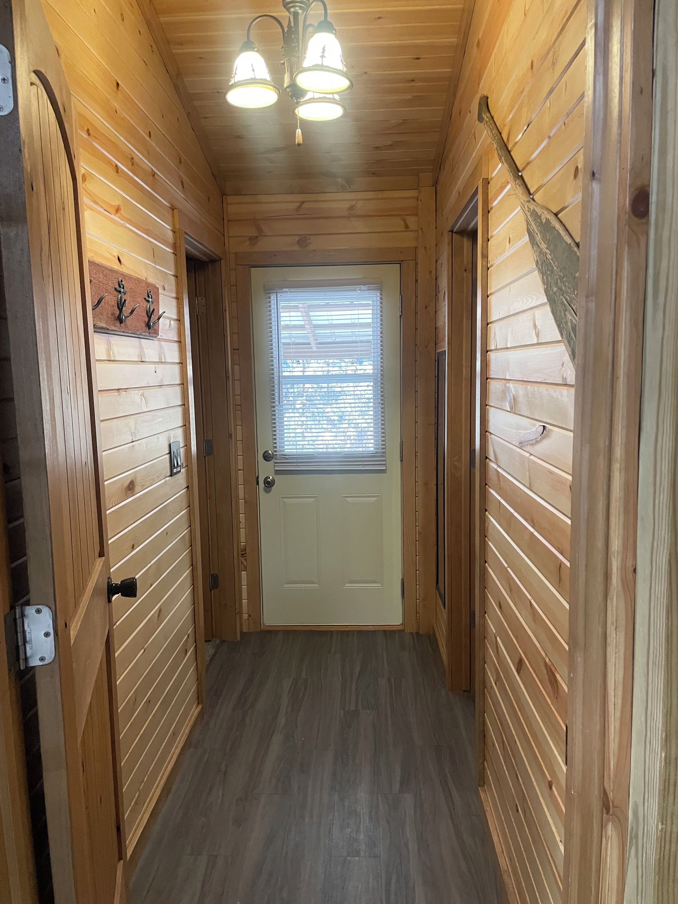 A wooden hallway with a white door, wooden walls, and a ceiling light fixture.