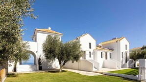 A white building with a tiled roof, a well-maintained lawn, and a clear blue sky.