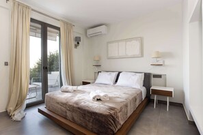 Ein modernes Schlafzimmer mit einem großen Bett, einer Glastür zum Balkon, zwei Nachttischen mit Lampen und einer Klimaanlage.
