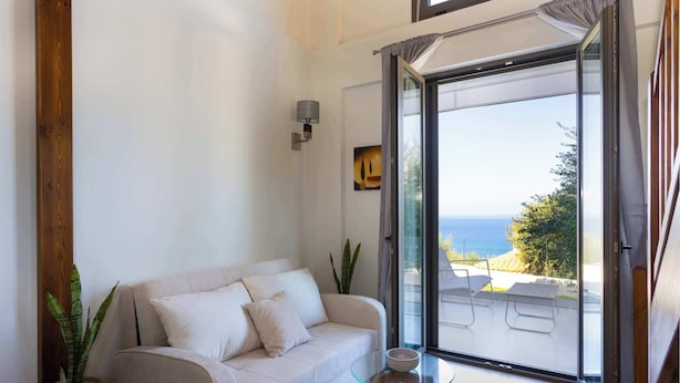 A modern living room with a sofa, a glass table, and a view of the sea through a sliding glass door. - Eneos Residence - Koroni Poolside Jewel (QXW3+7GQ Koroni, Greece)