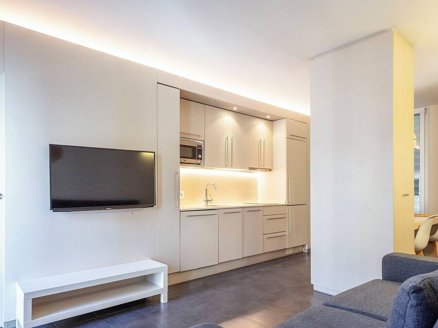 A modern kitchen with white cabinets, a built-in microwave, and a flat-screen TV mounted on the wall.