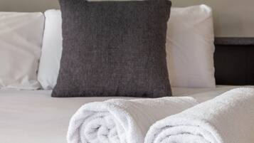A neatly made bed with white and gray pillows and two rolled white towels.