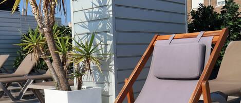 A sun lounger with a cushion, a potted plant, and a tiled patio area.