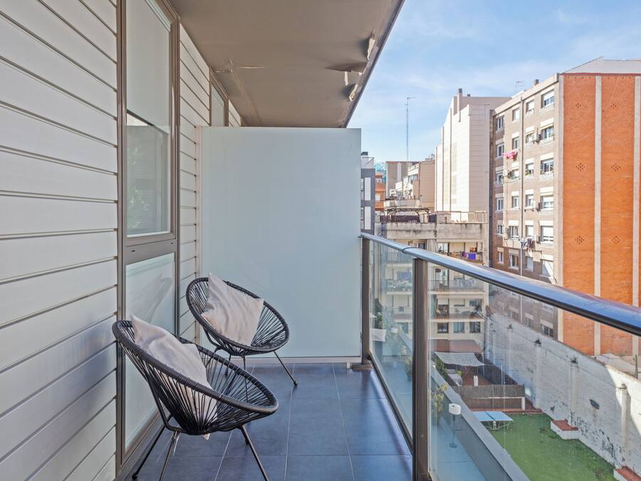 A balcony with two black wicker chairs and a glass railing overlooking a cityscape.