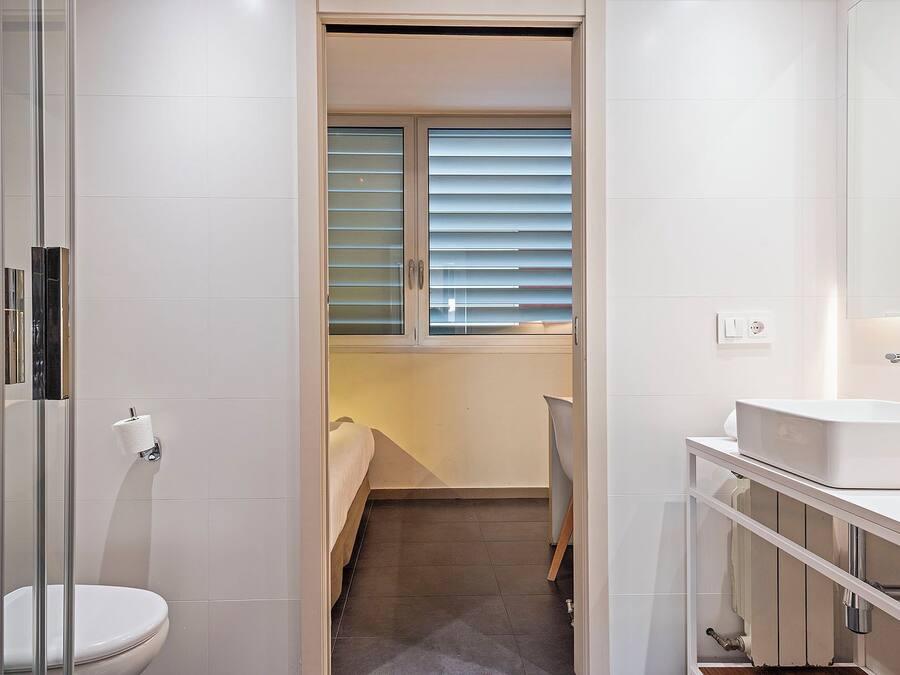 Un baño moderno con inodoro, cabina de ducha de vidrio, lavabo y ventana con persianas.