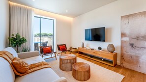 Ein modernes Wohnzimmer mit einer Couch, Sesseln, einem Fernseher und einem großen Fenster.
