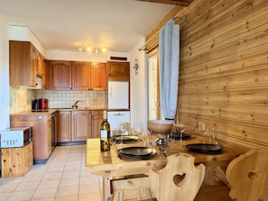 Una cocina con armarios de madera, una mesa de comedor dispuesta con platos, vasos y una botella de vino.
