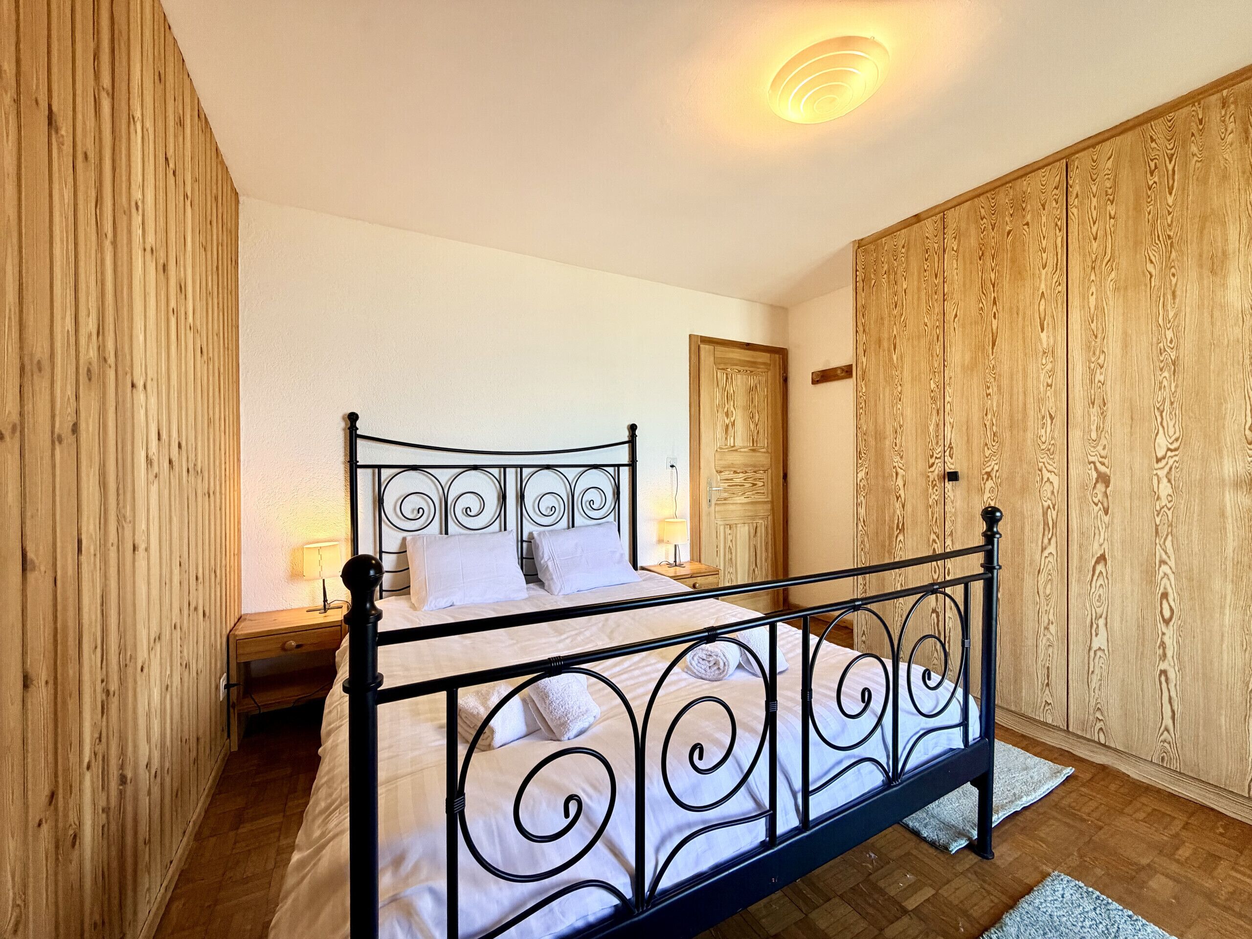 Une chambre à coucher avec un lit en métal, une armoire en bois et une table de chevet avec une lampe.